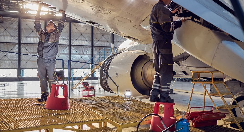 Tecnici di manutenzione al lavoro su ala e motore di un aeromobile in hangar